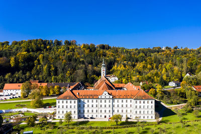 Houses and trees by buildings against clear blue sky