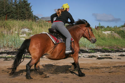 Woman riding horse on dirt road against sky