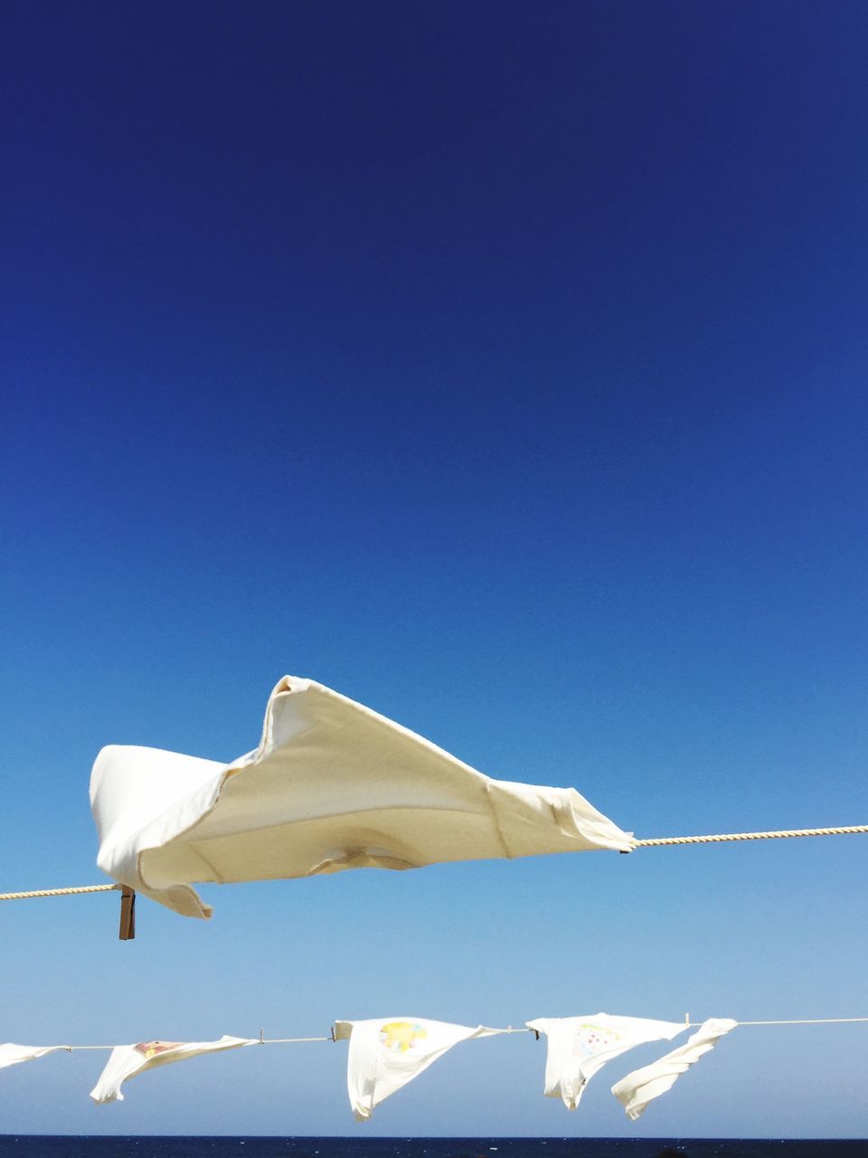 blue, low angle view, clear sky, white color, copy space, white, bird, no people, day, sunlight, outdoors, sky, nature, flag, fabric, hanging, high section, built structure, roof, part of