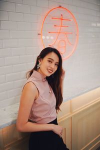 Portrait of smiling young woman standing against wall