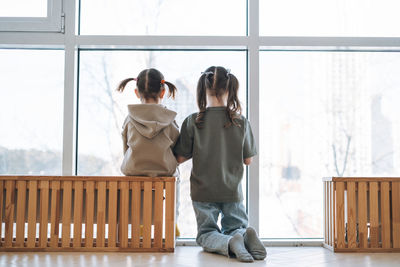 Cute little sisters girls looking in window at the home, people from behind