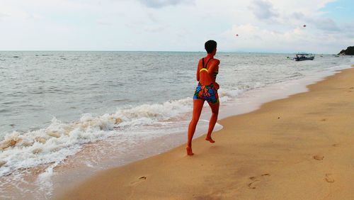 Rear view of man walking on beach against sky