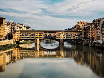 Arch bridge over river by buildings against sky