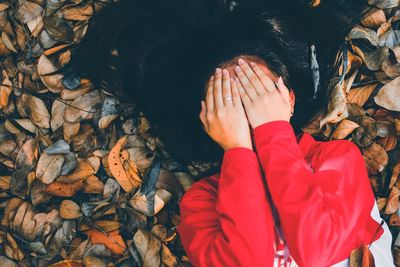 High angle view of woman covering face with hands while relaxing on field during autumn