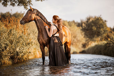 Woman and young horse standing in water next to each other enjoying the summer 