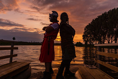 Rear view of couple walking on lake against sky during sunset