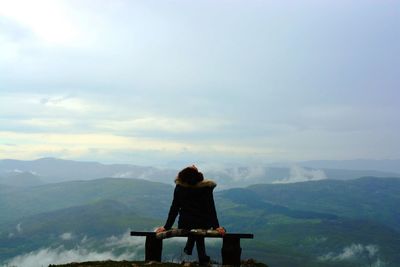 Rear view of man sitting on mountain against sky