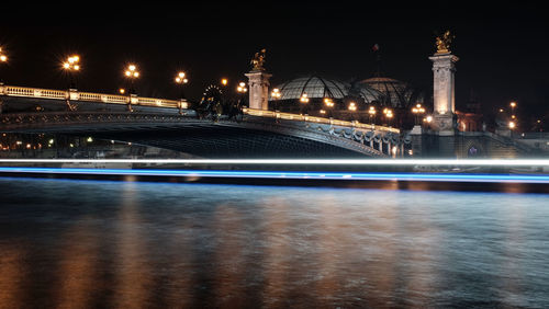 Illuminated bridge over river in city at night