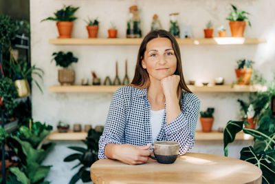 Attractive brunette woman 40s at the bar in a cozy shop with plants