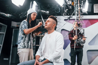 Young man is preparing for tv online broadcast. woman helps with make up.