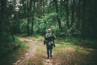 Rear view of man wearing uniform walking on footpath in forest