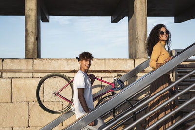 Young couple climbing stairs, carrying bicycle