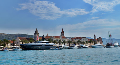 Sailboats in sea by buildings against sky