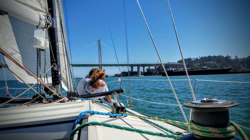 Couple sitting on sailboat in sea against sky