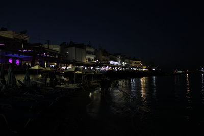 Illuminated buildings by river against sky at night