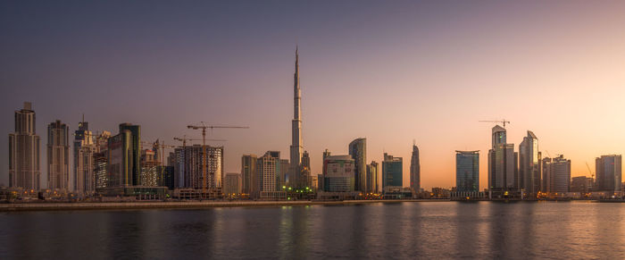 Sea against burj khalifa amidst towers against sky at sunset