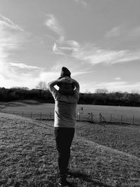 Rear view of father carrying son on shoulders against sky