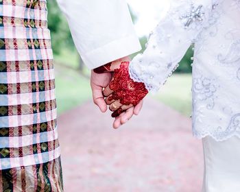 Midsection of bride and bridegroom holding hands on footpath