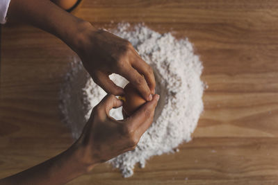 Cropped image of woman breaking egg in flour on table