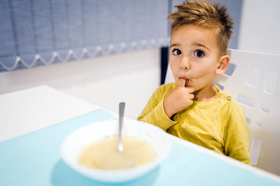 Portrait of cute boy with finger in mouth sitting by table