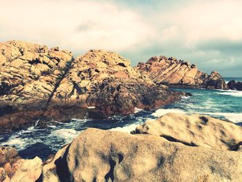 Rock formations in sea against cloudy sky