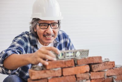 Mature man wearing hardhat making brick wall in workshop