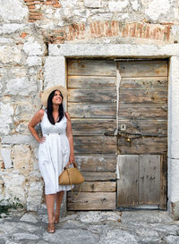Portrait of a young woman in white dress in front of old stone house, old door.