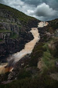 Scenic view of waterfall against cloudy sky