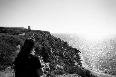 Rear view of woman standing on cliff against sea