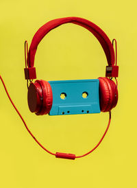 Old fashioned blue audio cassette in red headset showing concept of listening to music against yellow background in studio