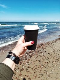 Midsection of woman holding drink at beach against sky