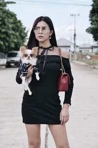 Portrait of woman wearing sunglasses with dog standing on road