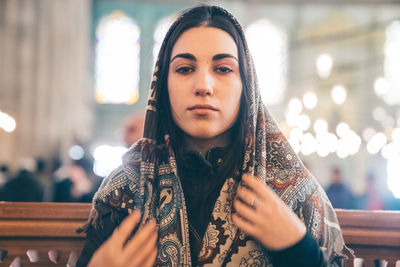 Portrait of beautiful young woman wearing scarf while sitting at mosque