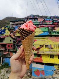 Cropped hand holding ice cream cone against houses