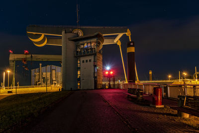 Empty road against illuminated buildings at night