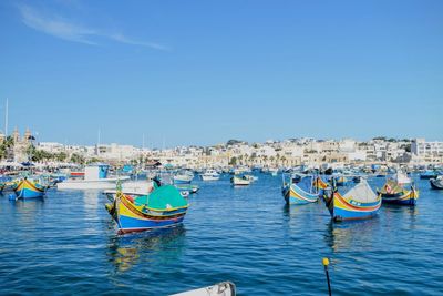 Boats moored at harbor against clear blue sky