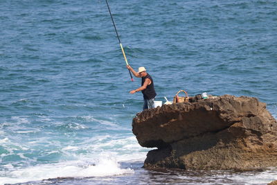 Man fishing on rock in sea
