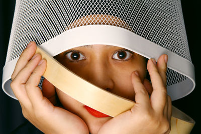 Close-up portrait of woman covering face with basket against black background