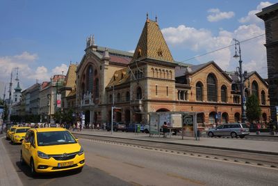 Vehicles on road by cathedral against sky in city