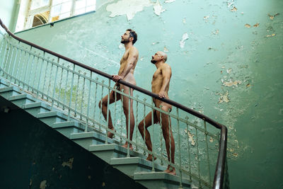 Full length of shirtless man and woman standing on railing