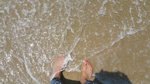 Low section of woman barefooted standing in ocean water on beach