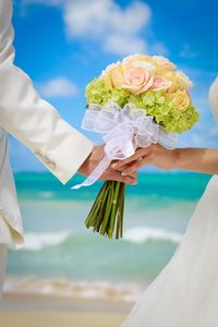 Cropped image of couple holding bouquet at beach