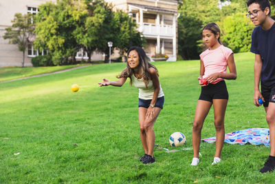 Woman throwing ball by son and daughter standing on grass