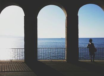 Full length rear view of woman standing by railing against sea