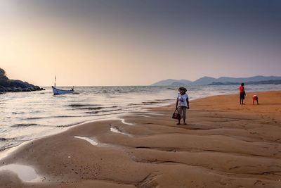 People at beach against clear sky during sunset