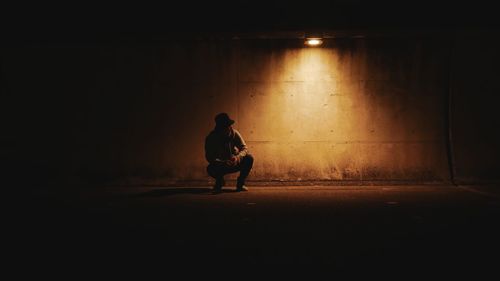 Man crouching on road against illuminated wall at night