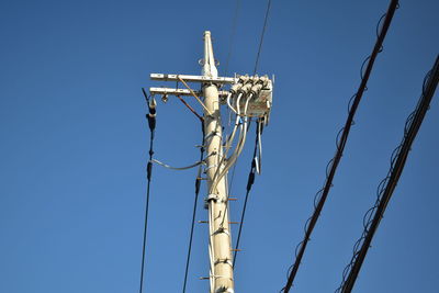 Low angle view of electricity pylon against clear blue sky