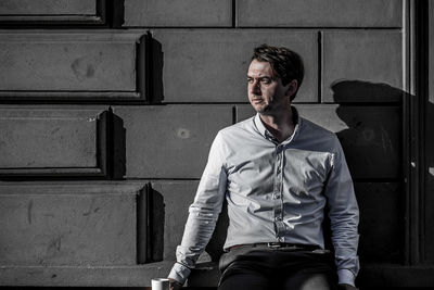 Man looking away while sitting against wall