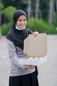 Portrait of smiling woman holding cake while standing outdoors