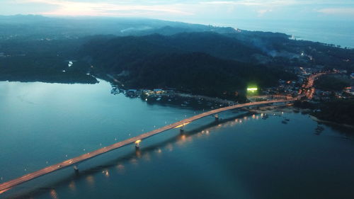 High angle view of illuminated city by sea against sky